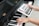A person is holding a tablet displaying a musical scale app over a piano keyboard. One hand is placed on the piano keys, and the other hand is holding the tablet screen which shows a detailed musical notation.