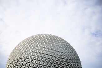 A geodesic dome structure rising against a rugged coastal backdrop under a cloudy sky.