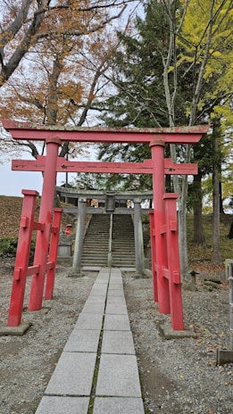 A vibrant red torii gate standing at the entrance of a serene Japanese shrine surrounded by autumn leaves.