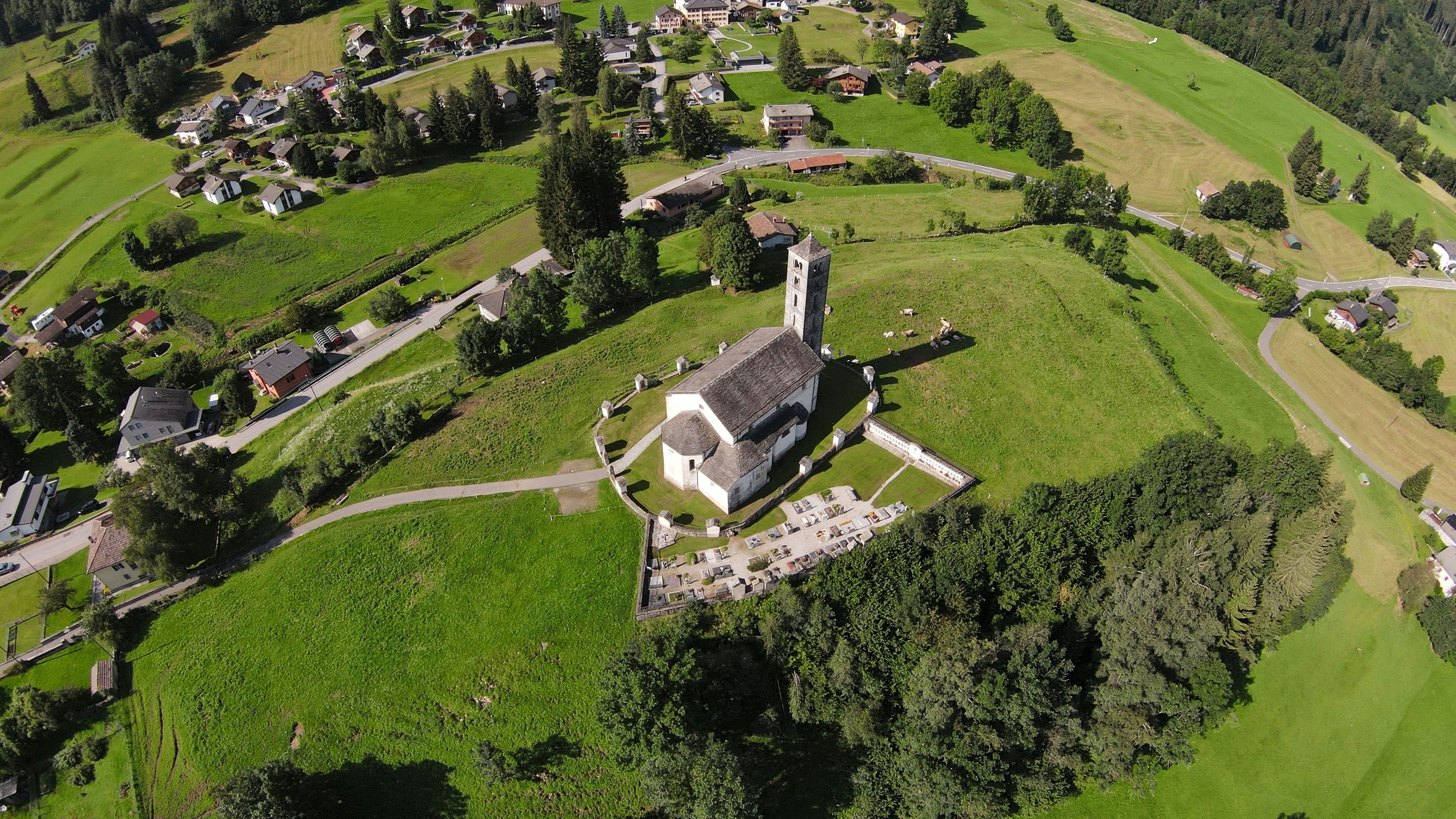 Aerial view of a quiet residential village with a church at its center surrounded by green fields.