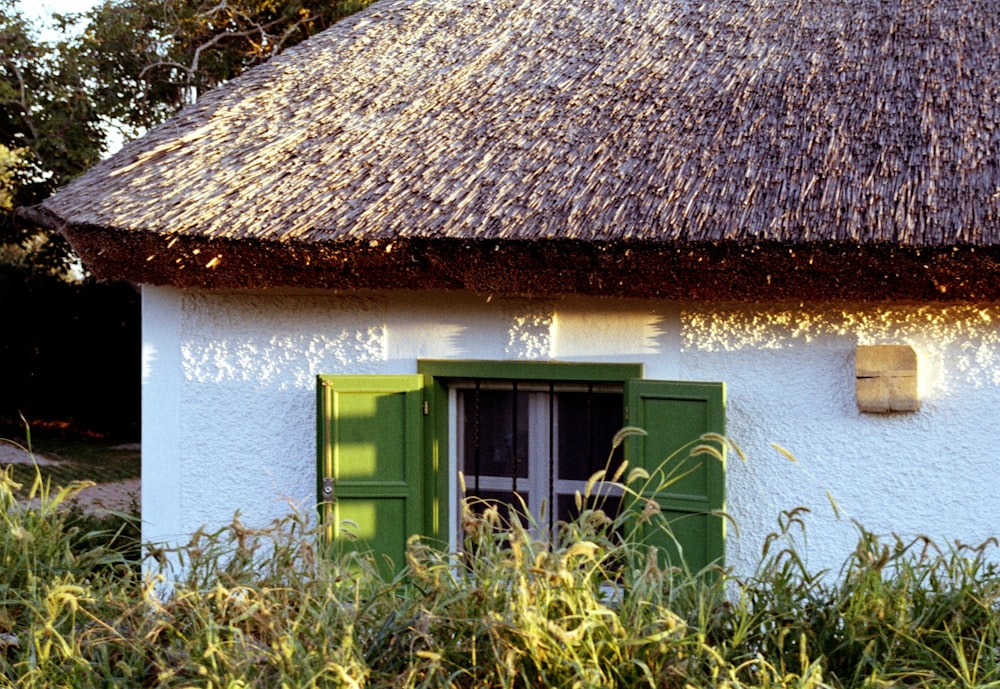 a white house with a thatched roof and green shutters