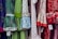 A colorful display of dresses with various polka dot and floral patterns. The fabrics feature a mix of vibrant colors including green, blue, red, and white. Ruffled sleeves and lace accents add texture, while price tags are visible hanging from some of the garments.