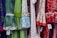 A colorful display of dresses with various polka dot and floral patterns. The fabrics feature a mix of vibrant colors including green, blue, red, and white. Ruffled sleeves and lace accents add texture, while price tags are visible hanging from some of the garments.