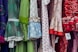 A colorful display of dresses with various polka dot and floral patterns. The fabrics feature a mix of vibrant colors including green, blue, red, and white. Ruffled sleeves and lace accents add texture, while price tags are visible hanging from some of the garments.