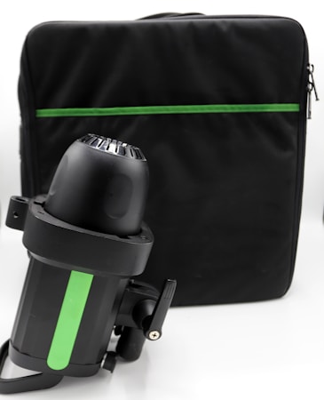 A black underwater scooter with a green stripe is positioned upright in front of a large black bag with a green accent zipper. The image features a simple, modern design with a focus on the scooter's contours and details.