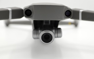 Close-up view of a drone's front, featuring two cameras on either side with a prominent central lens, positioned against a neutral background.