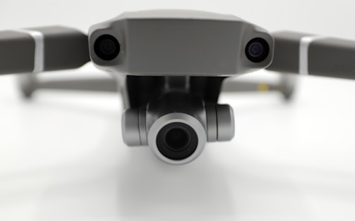 Close-up view of a drone's front, featuring two cameras on either side with a prominent central lens, positioned against a neutral background.