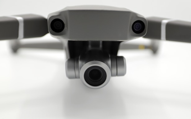 Close-up view of a drone's front, featuring two cameras on either side with a prominent central lens, positioned against a neutral background.