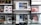 A store shelf filled with various boxed electronic items, including lenses and cameras, arranged in an orderly fashion. In the foreground, there is an empty frame-like object, possibly a camera accessory, placed on a reflective glass surface.
