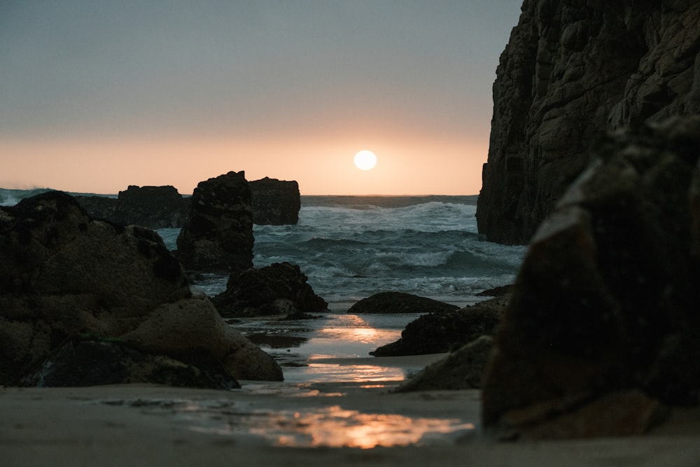 the sun is setting over the ocean and rocks