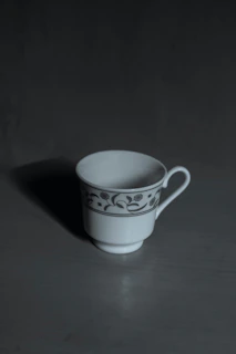 A white ceramic cup with delicate red patterns resting on a black cloth.