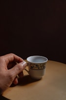 Close-up of a hand gently holding a small, aged porcelain tea cup with a crackled glaze.