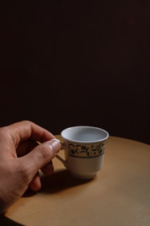 Close-up of a hand gently holding a small, aged porcelain tea cup with a crackled glaze.