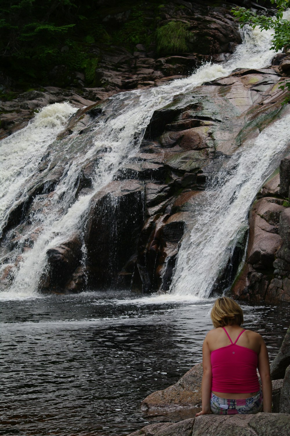 a woman sitting on a rock next to a waterfall