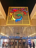 A bustling shopping mall exterior with people entering and exiting.