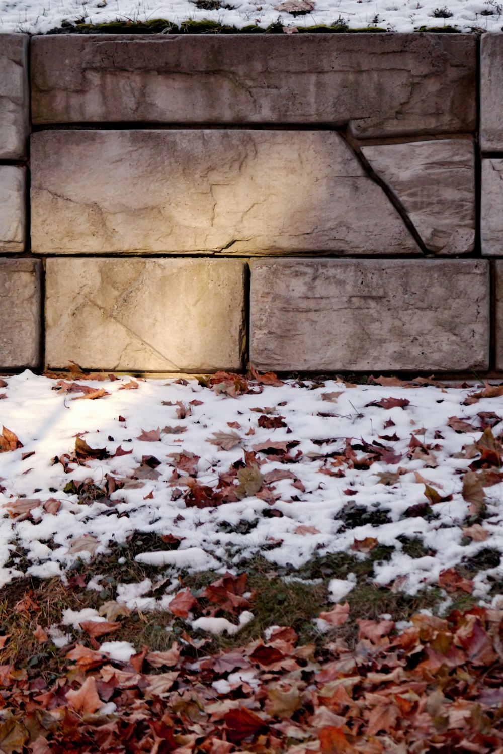 a fire hydrant in front of a brick wall covered in snow