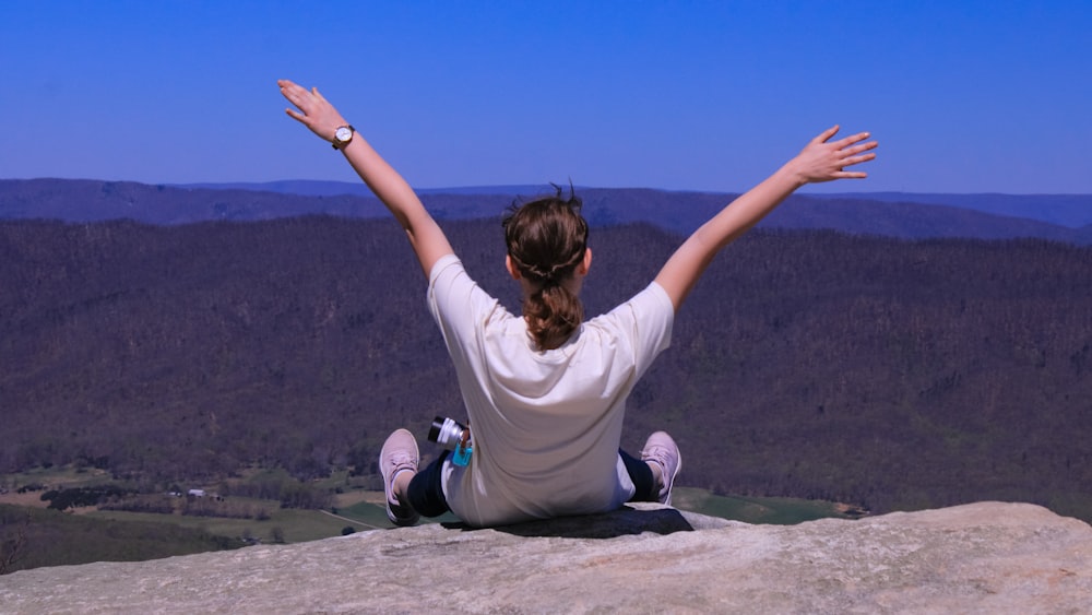 a woman sitting on top of a rock with her arms outstretched
