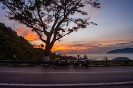 Sunset view with motorcycles parked beside a calm lake reflecting orange hues.