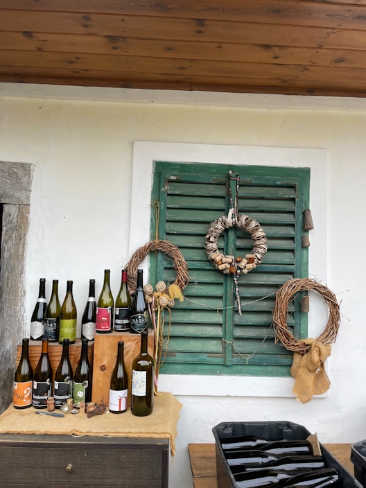 A rustic wooden table displaying several bottles of handmade wine with a backdrop of lush Şirince vineyards.