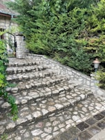 Custom stone steps leading up to a charming front porch surrounded by greenery.