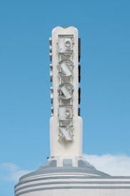 A tall, vertical sign with the word 'FOX' displayed in large, bold letters. The sign is mounted on a sleek, art-deco style building, featuring a clean and minimalist design with off-white and soft gray tones. The background is a clear blue sky.