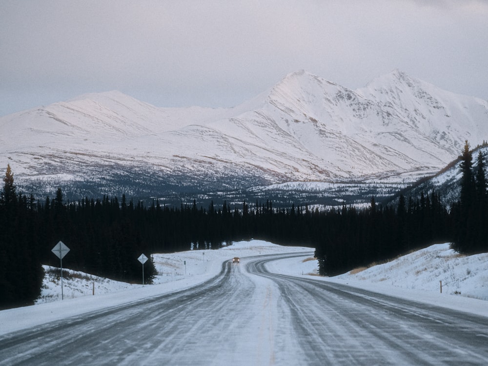 a snow covered road with mountains in the background