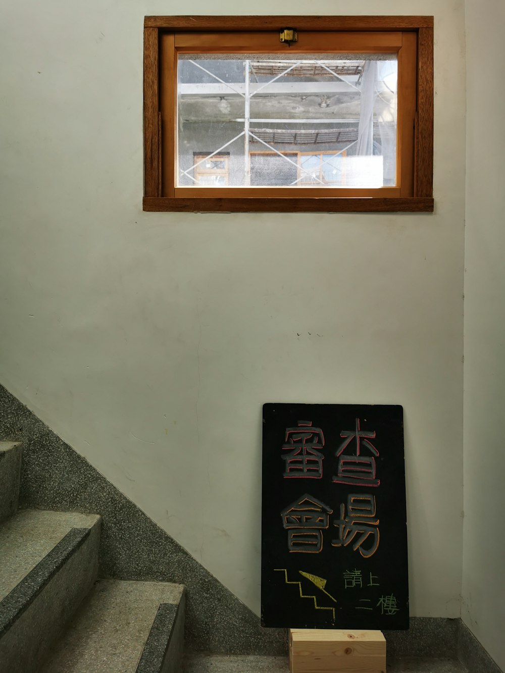 a sign sitting in front of a window next to a set of stairs