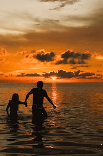 A cinematic wide shot of a couple holding hands, walking along a riverside at sunset with vibrant colors enhanced.