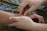Two hands gently hold and press the wrist of another person, suggesting a massage or therapeutic touch. The background features a patterned fabric with blue and green tones.