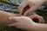 Two hands gently hold and press the wrist of another person, suggesting a massage or therapeutic touch. The background features a patterned fabric with blue and green tones.