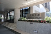 Entrance to an office building with a sign for Fairmont House. The area is clean and modern, featuring granite pillars, glass doors, and flower beds with vibrant red flowers.