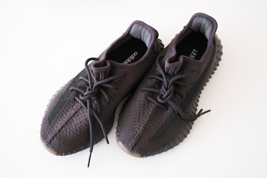 A pair of dark-colored knitted sneakers with thick rubber soles and detailed stitching. The shoes have black laces and a breathable fabric design. The insoles display logos.