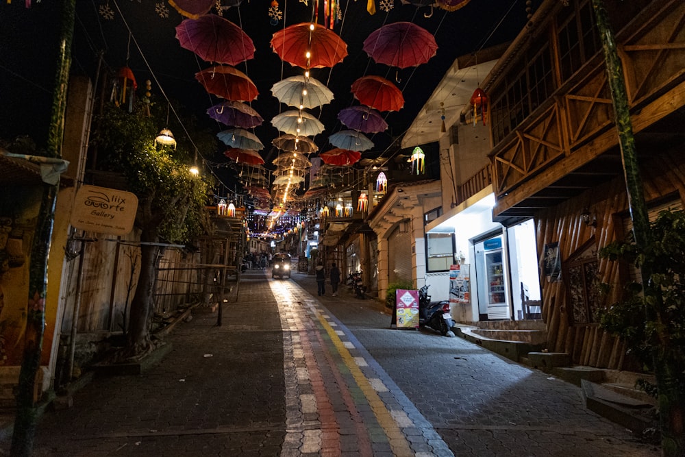 a narrow street with umbrellas hanging from the ceiling