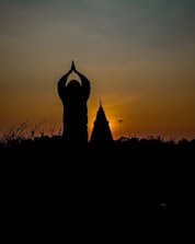 A peaceful image of a person meditating under a maroon sky at dusk.