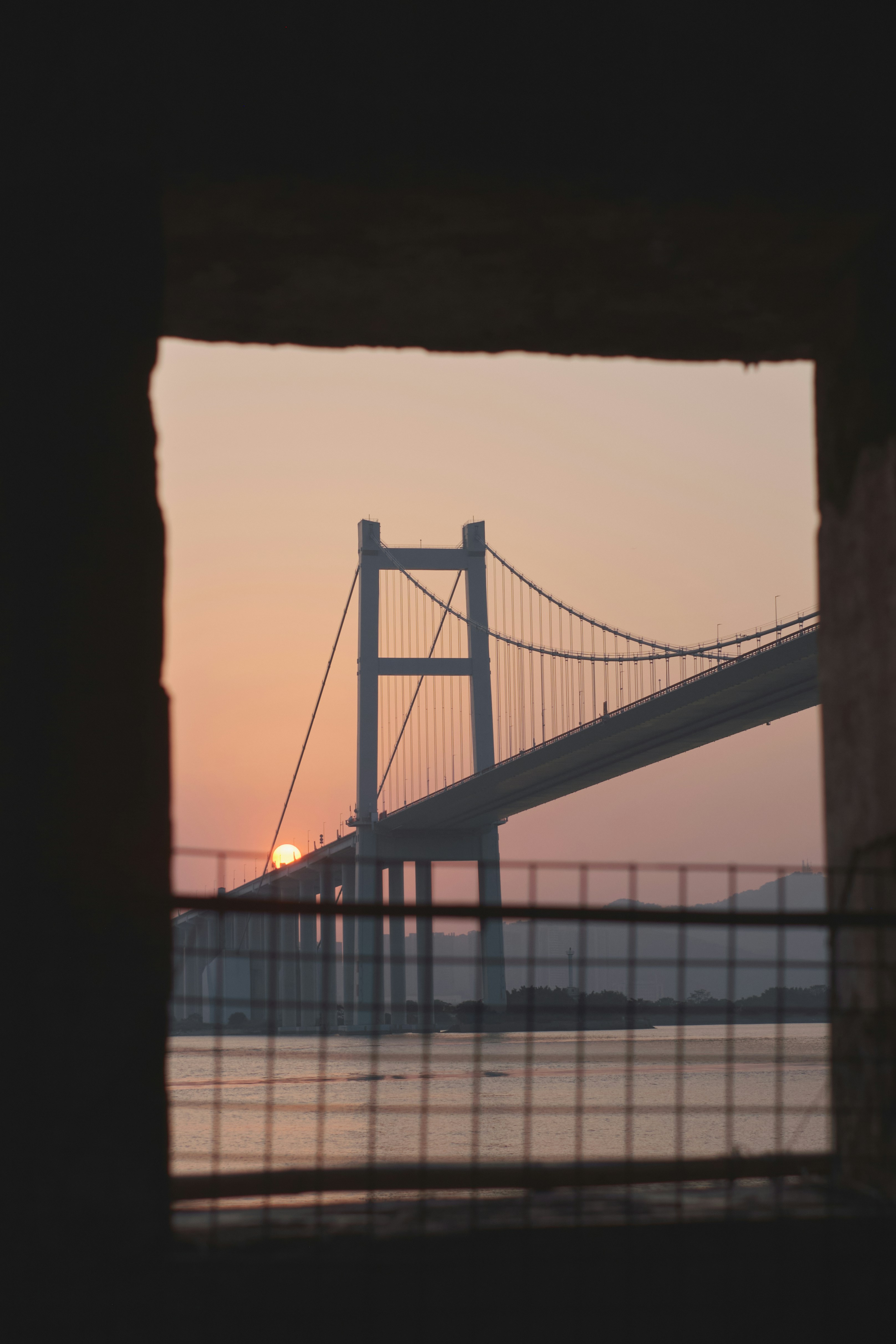 the sun is setting behind a bridge over a body of water