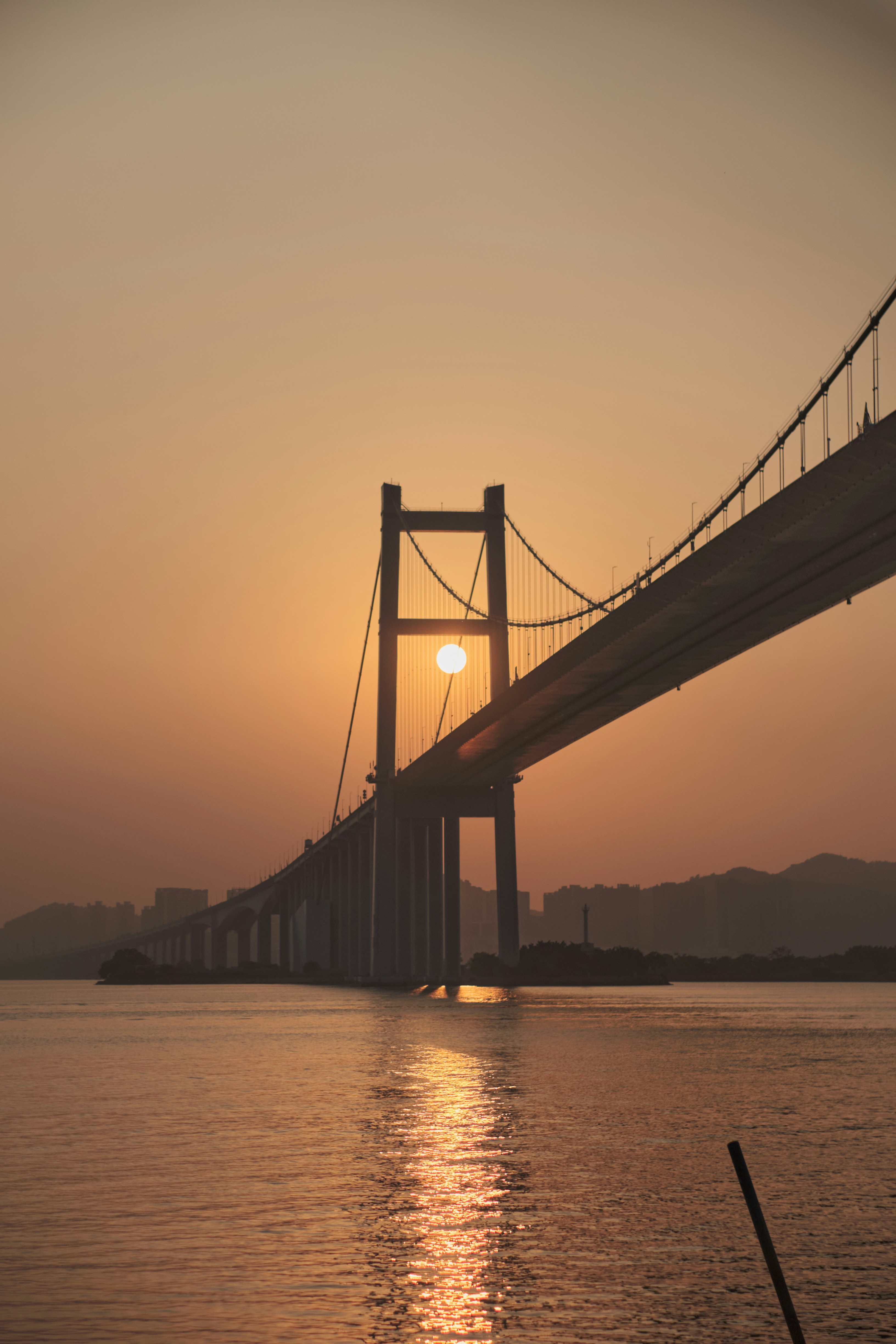 the sun is setting behind a bridge over the water