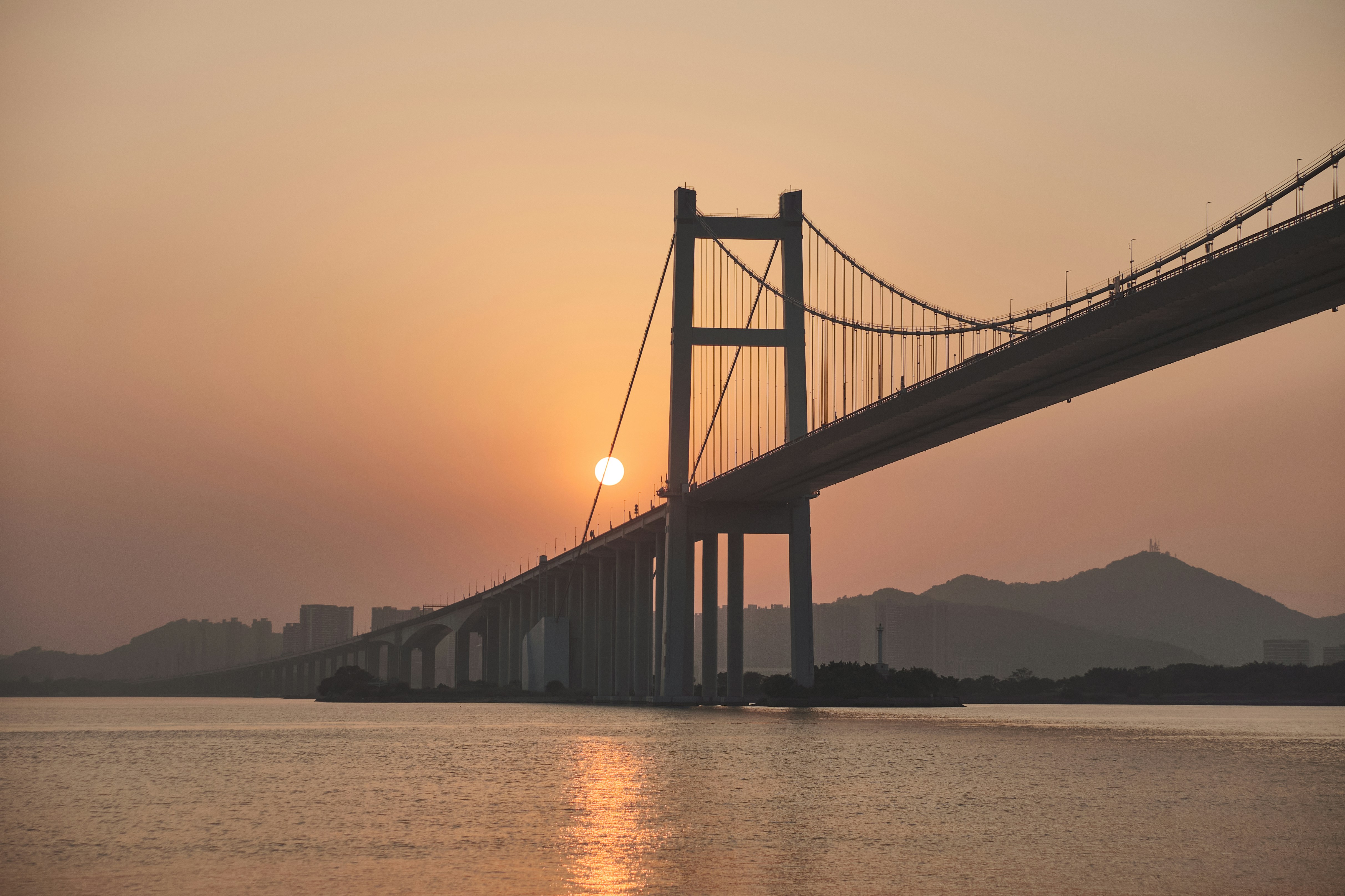 the sun is setting behind a bridge over the water