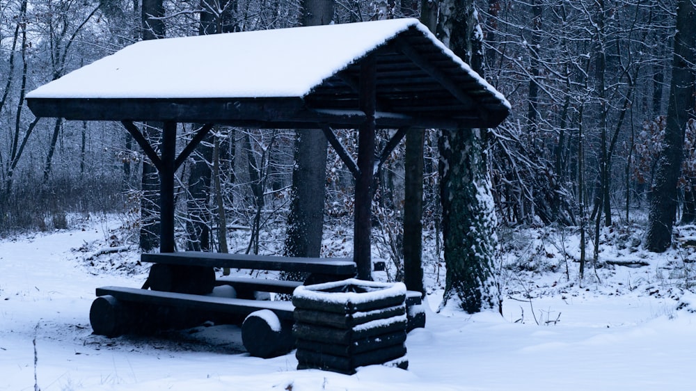 a covered picnic table in the middle of a snowy forest
