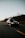 A black car with a roof box is traveling along a deserted highway, surrounded by bare trees and a clear sky at dusk.