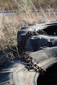 Large, heavy-duty tires lie in a field of dry grass. Thick metal chains are draped over them, suggesting they are secured or part of some equipment.