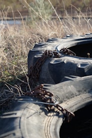 Large, heavy-duty tires lie in a field of dry grass. Thick metal chains are draped over them, suggesting they are secured or part of some equipment.