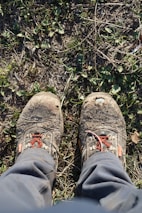 Close-up of trekking boots on a rugged trail with wildflowers around.