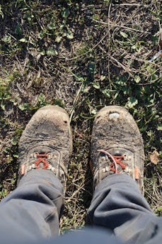 Close-up of trekking boots on a rugged trail with wildflowers around.