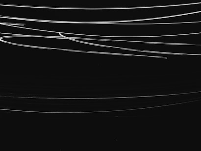 Thin, white curved lines gracefully streak across a dark black background, creating a sense of fluid motion.