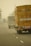 Several trucks are seen driving along a foggy highway. The back of a prominent yellow truck is visible with some signage and markings. The road has marked lanes, and the fog creates a hazy atmosphere, obscuring the distance.