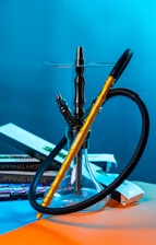 A hookah with a golden and black hose is prominently placed against a vibrant blue background. Books with titles related to 'flipping houses' and colorful packaging are casually arranged around the base.
