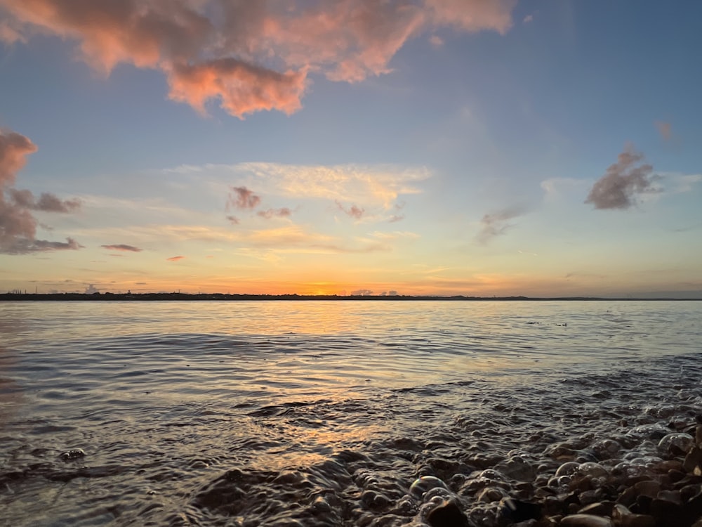 a sunset over a body of water with rocks in the foreground