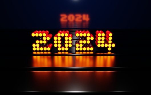 A glowing digital display showing the number 2024 in bright orange lights, set against a dark background with a reflective surface.