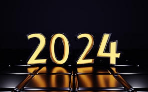 Large, bold numerals forming the year 2024 in a bright, glowing yellow hue against a dark, reflective background. The numbers appear three-dimensional and are mirrored on the shiny surface below.
