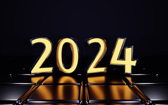 Large, bold numerals forming the year 2024 in a bright, glowing yellow hue against a dark, reflective background. The numbers appear three-dimensional and are mirrored on the shiny surface below.